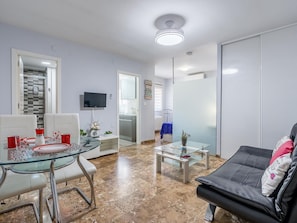 A modern living room with a glass dining table, a sofa, and a television mounted on the wall. - Central renovated studio - Stay in Granada (Granada)