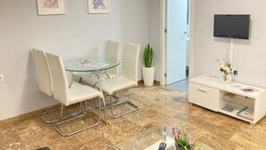A modern room with a glass table, white chairs, a potted plant, a TV, and a bookshelf. - Central renovated studio - Stay in Granada (Granada)