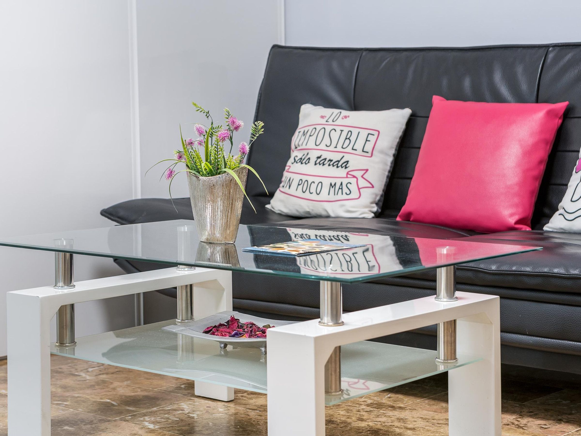 En moderne stue med et glasbord, en sort lædersofa og pyldepuder.