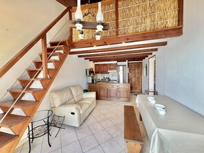 A spacious living area with a wooden staircase, a sofa, a dining table, and a kitchen in the background. - Apartment with stunning sea view - 4 guests (Casaglione-Tiuccia)