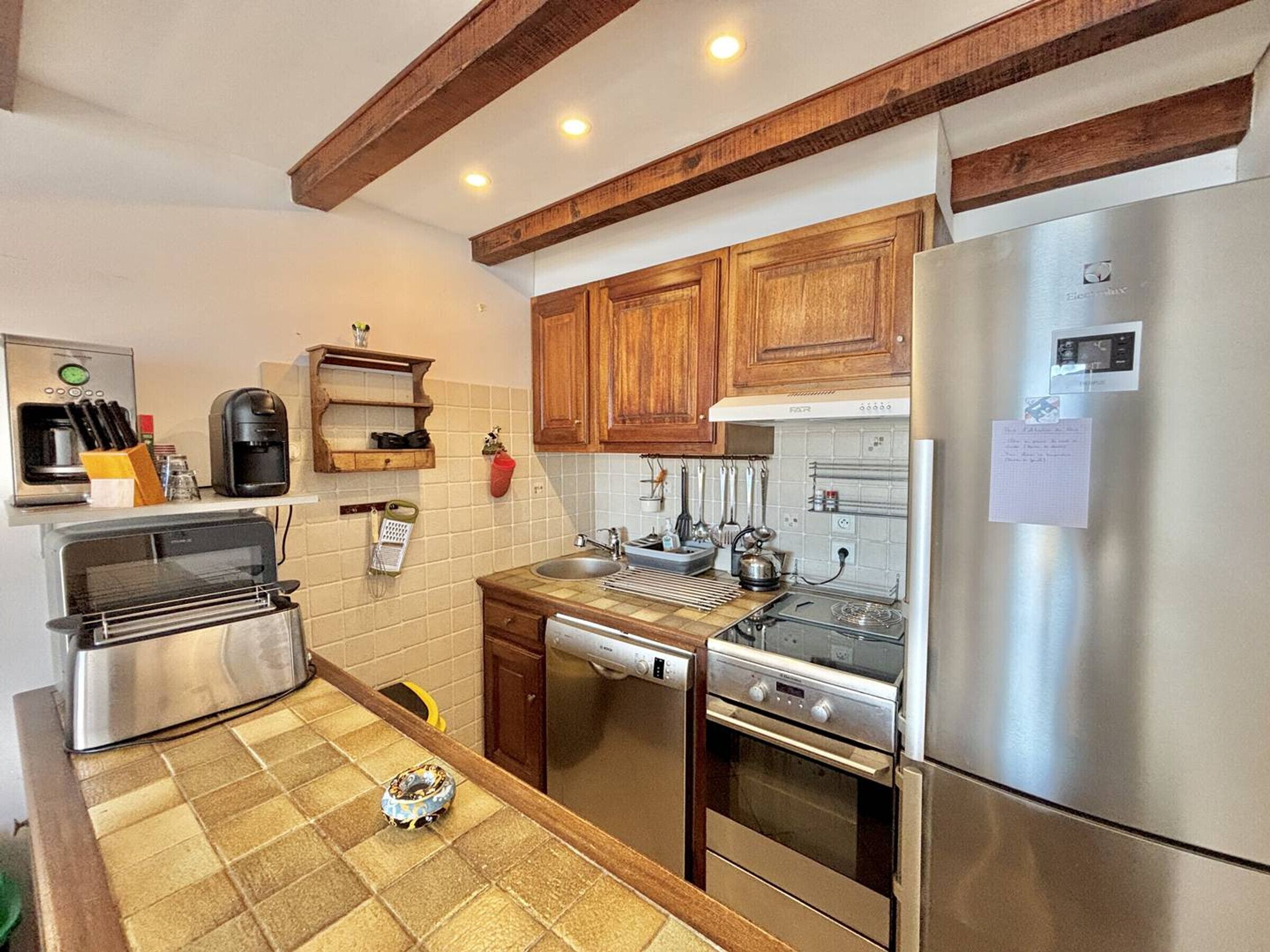 Una cocina con armarios de madera, un refrigerador de acero inoxidable, una cafetera, un tostador y un hervidor.