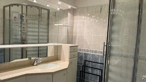 Een badkamer met een douchecabine van glas, een wastafel met spiegel, en betegelde wanden.