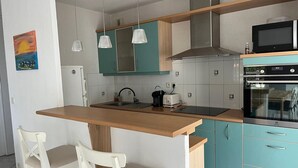 Een moderne keuken met een centraal eiland, twee stoelen, een magnetron, een oven en hangende lampen.