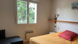 Een slaapkamer met een bed, nachtkastje, verwarming, raam en een schilderij aan de muur.