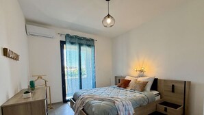Un dormitorio con cama, mesitas de noche, una lámpara colgante y una ventana con cortinas.