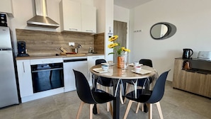 Una cocina moderna con armarios blancos, una campana extractora de acero inoxidable y un comedor con una mesa redonda y sillas negras.