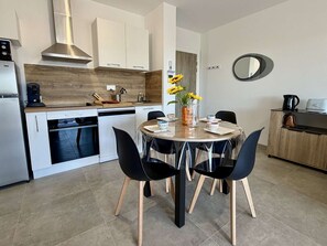 Een moderne keuken met witte kasten, een roestvrijstalen afzuigkap en een eethoek met een ronde tafel en zwarte stoelen.