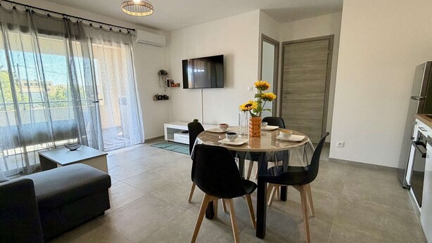 Una sala de estar moderna con comedor, sofá, televisor montado en la pared y zona de cocina.