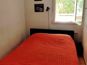 Uma cama de solteiro com cabeceira preta e colcha laranja em quarto com paredes brancas.