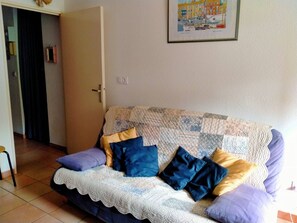 A living room with a sofa, pillows, a door, and a framed picture on the wall. - Air-conditioned apartment near beaches - 4 guests (Bormes-les-Mimosas)