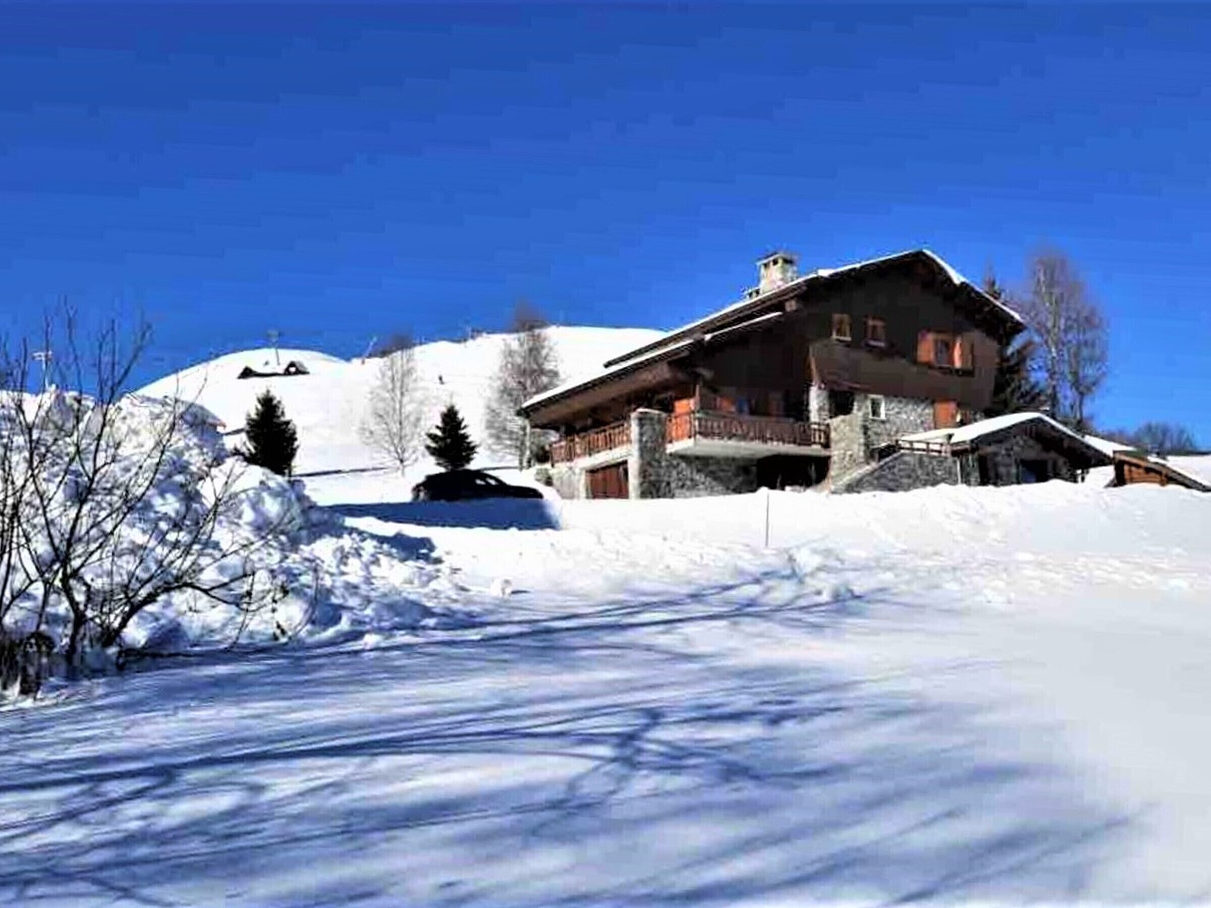 Un edificio grande de piedra de varios pisos con techo inclinado, rodeado de terreno y árboles cubiertos de nieve.