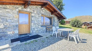 A stone building with wooden beams, a wooden door, and a window. There is a table and chairs outside. - Apartment with panoramic view - 8 guests (La Toussuire)