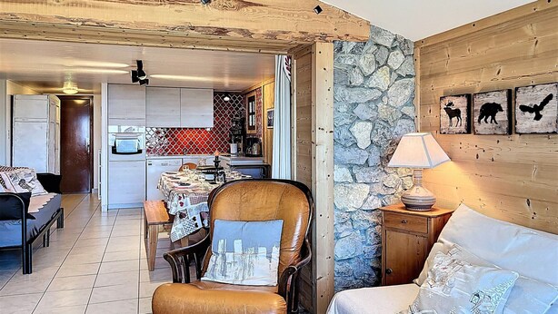A cozy living room with a fireplace, a dining area, and a kitchen with stone walls. - Apartment with panoramic view - 8 guests (La Toussuire)