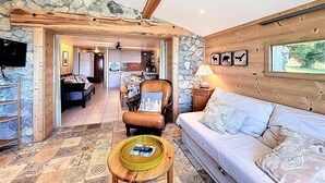 A cozy living room with a stone wall, wooden beams, a sofa, a coffee table, and a dining area with a table and chairs. - Apartment with panoramic view - 8 guests (La Toussuire)