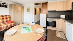 A compact kitchen with a dining area, a sofa, and a refrigerator. - Studio for 4 guests, center station south (La Toussuire)