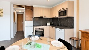 A modern kitchen with wooden cabinets, a microwave, a dishwasher, and a dining area with a table set for two. - Studio for 4 guests, center station south (La Toussuire)