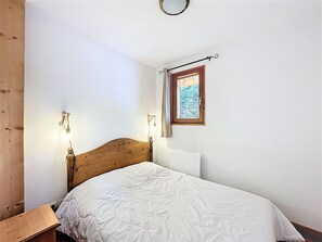 Ein Schlafzimmer mit einem hölzernen Kopfteil, einer weißen Bettdecke, einem Nachttisch, einer Wandlampe und einem Fenster mit Blick auf eine verschneite Landschaft.