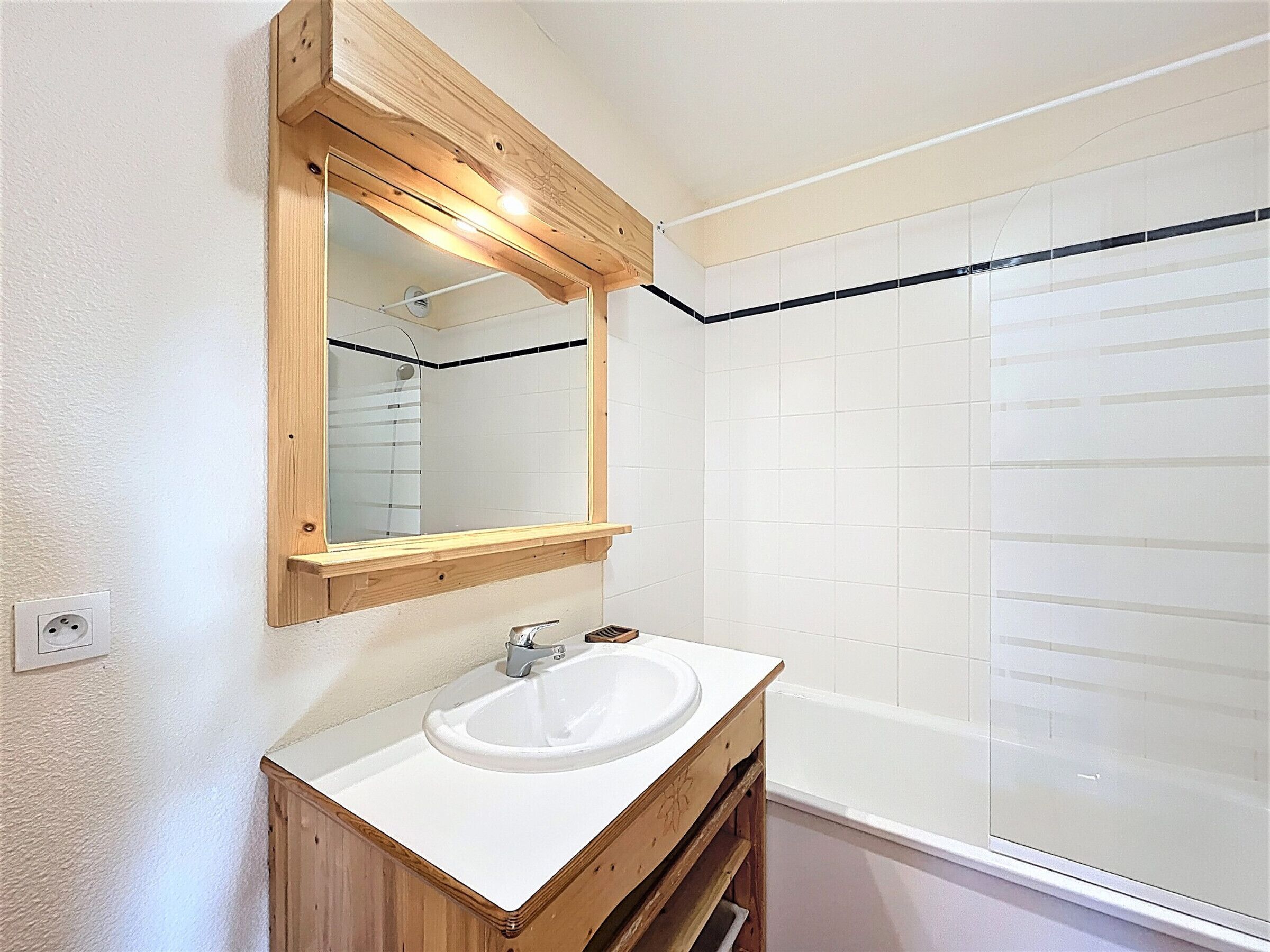 A bathroom with a wooden vanity, a white sink, a mirror, and a shower area.