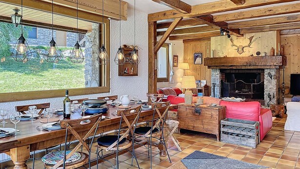 Een rustiek interieur met een eethoek, houten balken, een open haard en een stenen muur.