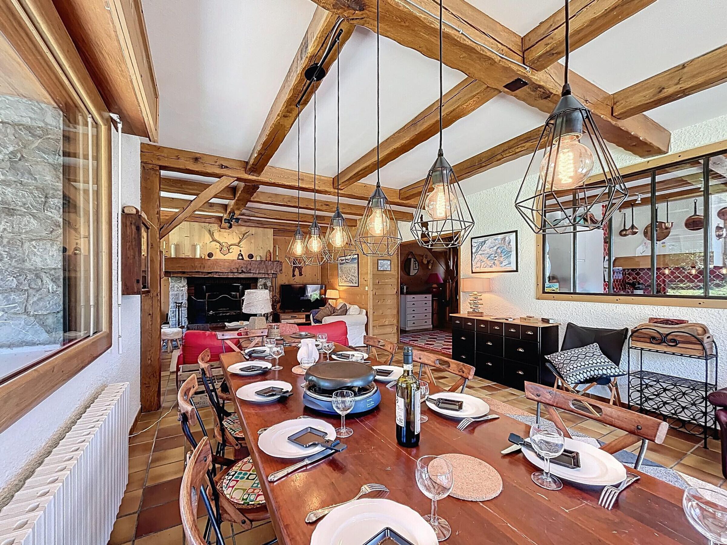 A spacious dining area with a long wooden table set for a meal, surrounded by wooden beams and hanging light fixtures.