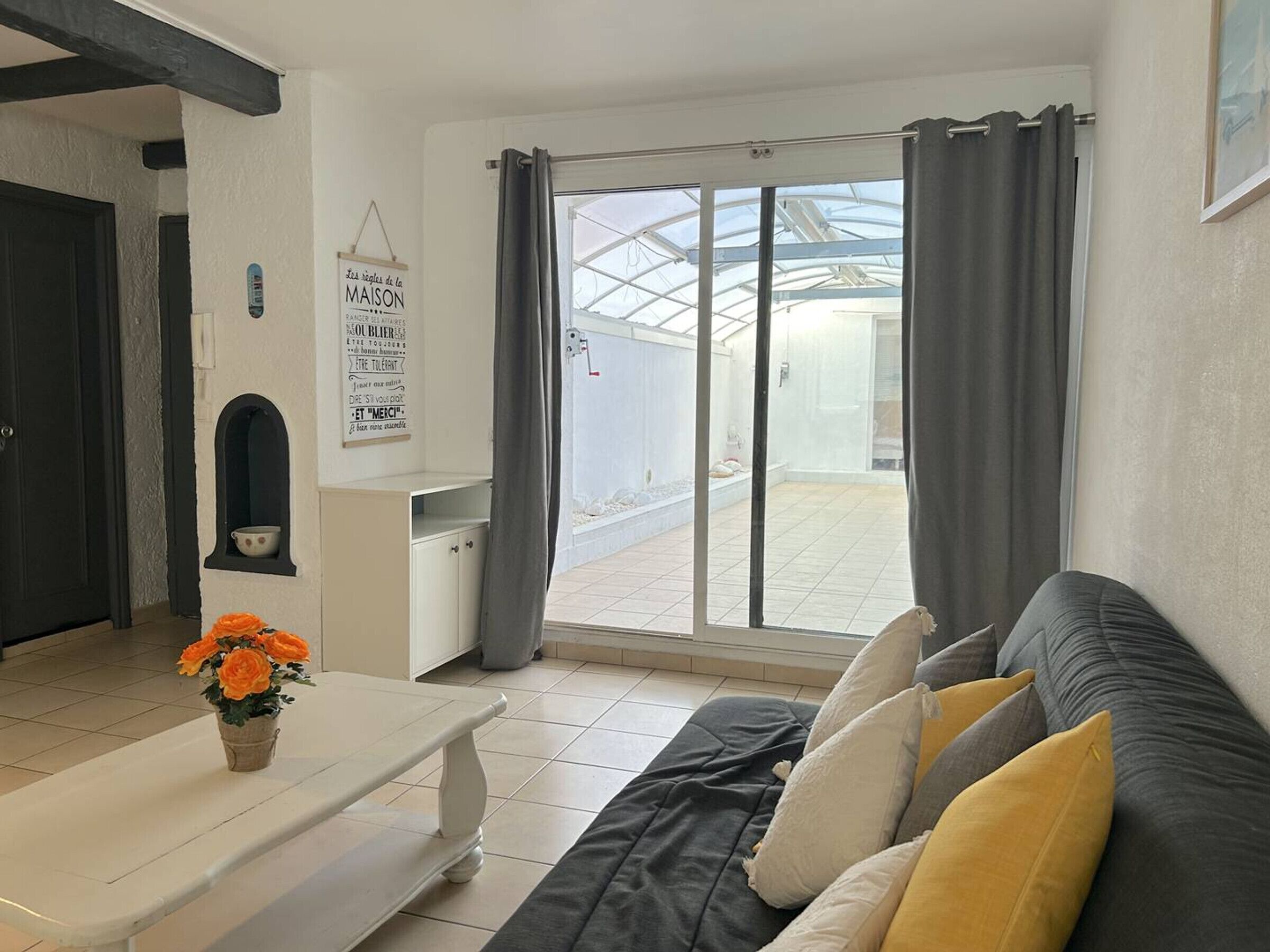 A living room with a sofa, a small table with a vase, a window with curtains, and a sign on the wall.