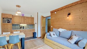 Un espacio habitable compacto con kitchenette, un comedor con sillas y una mesa, y un sofá con cojines.
