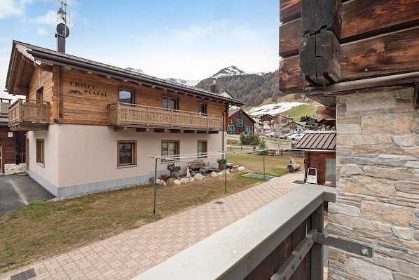 A chalet-style building with a balcony, a stone wall, and a mountain backdrop.