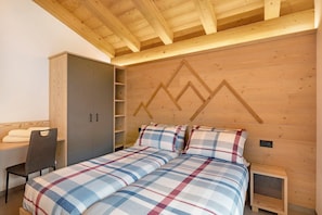 A bedroom with a bed, a chair, a wardrobe, and a wooden ceiling.