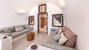 A modern living room with a sofa, a coffee table, and a view of a bedroom through an archway. - Pura Vida Cave House (Santorini)