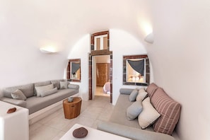 A modern living room with a sofa, a coffee table, and a view of a bedroom through an archway. - Pura Vida Cave House (Santorini)