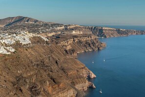 A coastal town with white buildings, cliffs, and a clear blue sea. - Pura Vida Cave House (Santorini)
