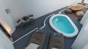 A rooftop terrace with a hot tub, lounge chairs, a table with chairs, and a small garden area. - Pura Vida Cave House (Santorini)