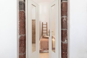 A narrow hallway with a bed, a wooden ladder, and a door leading to another room. - Pura Vida Cave House (Santorini)