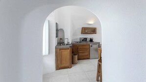 A compact kitchen with a microwave, sink, and wooden cabinets, under a white archway. - Pura Vida Cave House (Santorini)