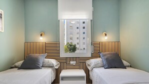 A twin room with two beds, a small bedside table, a window with a view of buildings, and wall-mounted lights. - Apartment 'Salou Beach' with Sea View, Wi-Fi, and Air Conditioning (Salou)