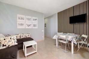 Ein Wohnzimmer mit einer Couch, einem kleinen Tisch, einem Esstisch mit Stühlen, einem flachbildfernseher an einer gestreiften Wand und gerahmten Kunstwerken.