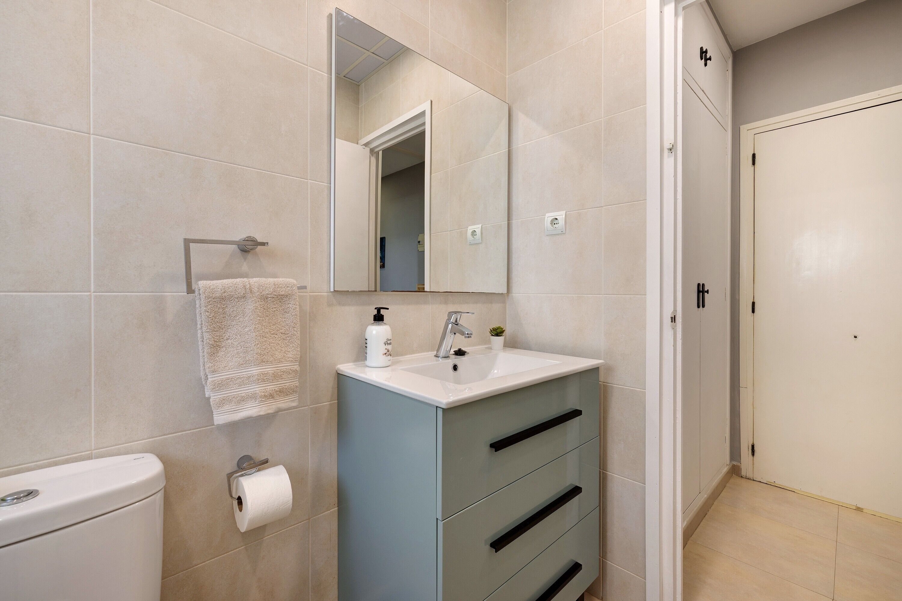 A bathroom with a toilet, sink, mirror, towel rack, and a cabinet with drawers.