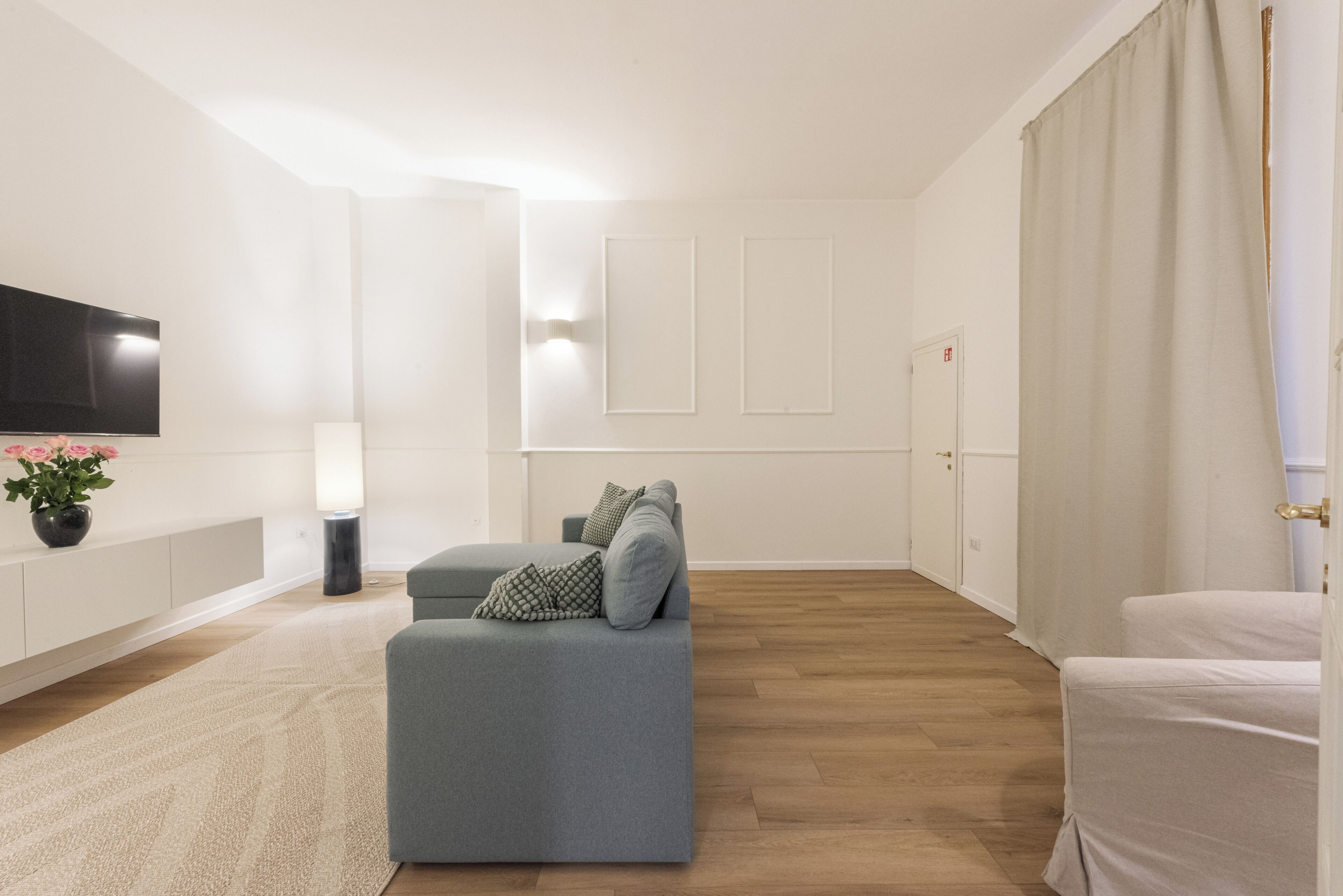 Een moderne woonkamer met een grijze bank, een flatscreen televisie, een lamp en een potplant.