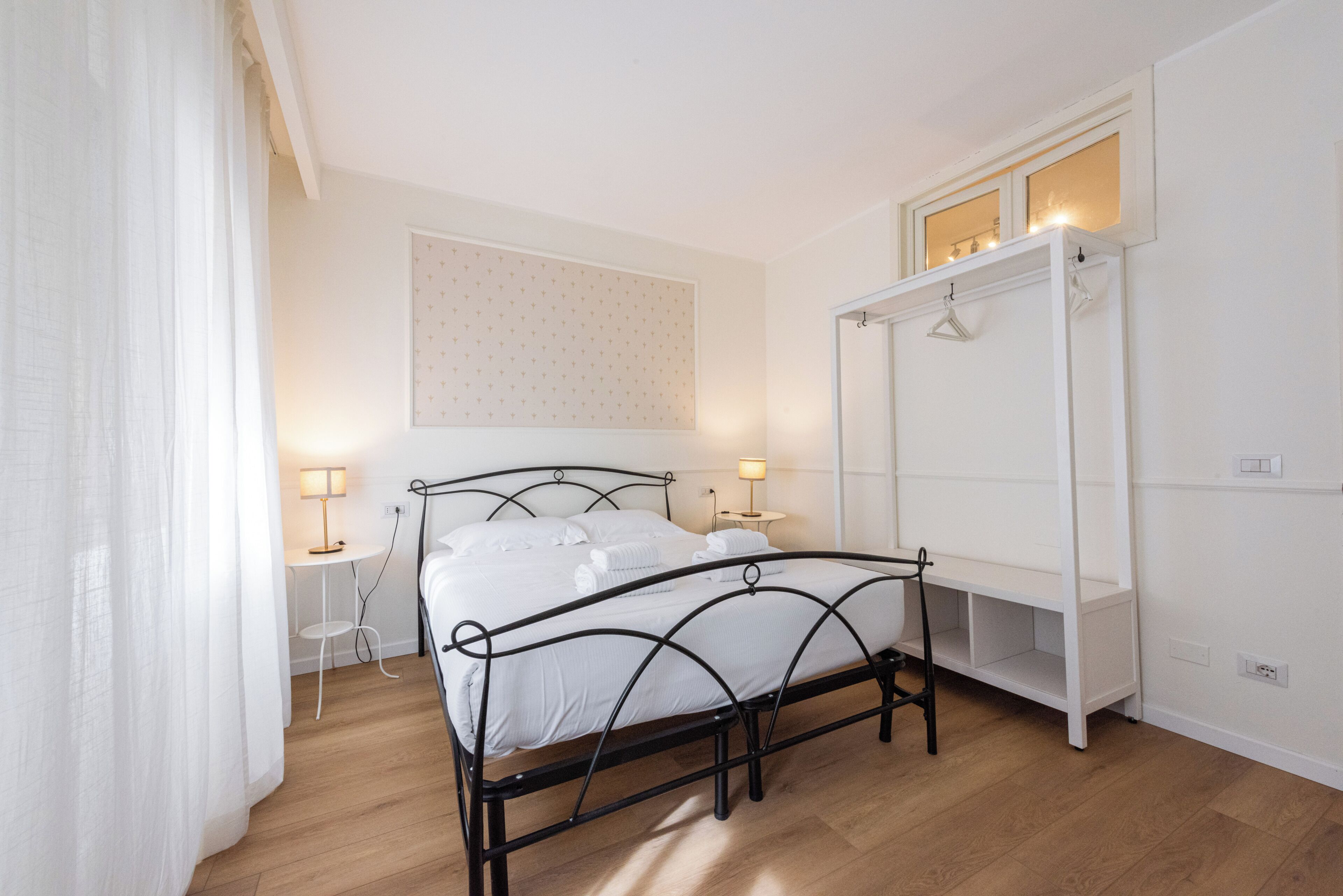 A bedroom with a bed, bedside tables, a hanging wardrobe, and a wall-mounted light fixture.