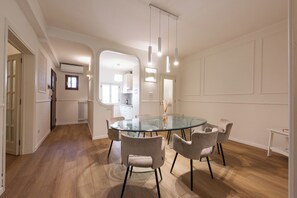 A modern dining area with a glass table, six chairs, pendant lighting, and a view into a kitchen. - Ognissanti Prestige by MMega (Florence)