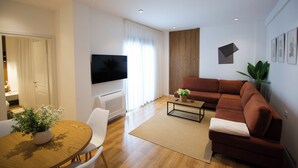 Una sala moderna con un sofá, un televisor de pantalla plana, una mesa de comedor con sillas y una planta en maceta.