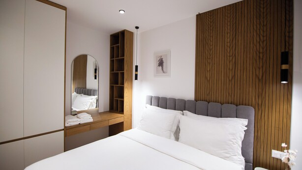 Un dormitorio moderno con una cama grande, un armario de madera, un espejo y una mesita de noche.