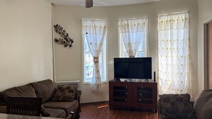 A living room with a ceiling fan, a flat-screen TV on a wooden cabinet, a brown sofa, and a dining table with chairs. - Move-In Ready 2BR Apartment – Clean, Cozy & Conveniently Located (Brooklyn)