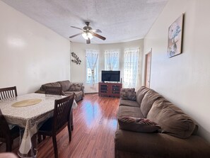 A living room with a dining table, sofas, a TV, and a ceiling fan. - Move-In Ready 2BR Apartment – Clean, Cozy & Conveniently Located (Brooklyn)