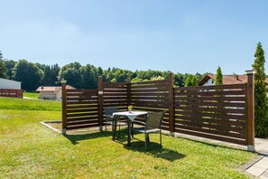 Un espacio al aire libre cercado con una mesa y sillas, rodeado de vegetación y un cielo despejado.
