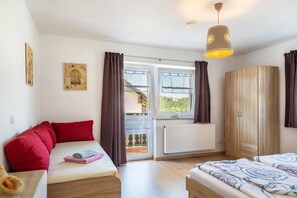 Una habitación con cama, sofá, armario, ventana con cortinas y una lámpara en el techo.