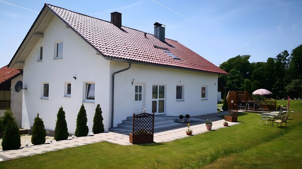 A two-story house with a red-tiled roof, white exterior walls, and a front porch with steps leading to the entrance.