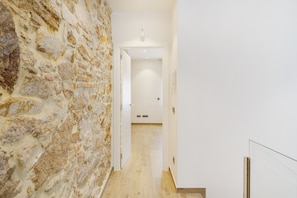 Un pasillo con pared de piedra, suelo de madera y una puerta blanca al final.