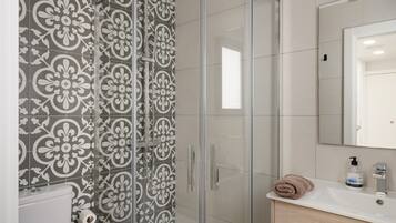 A bathroom with a shower, toilet, sink, and mirror.