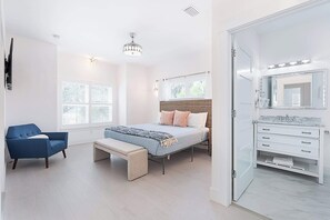A bedroom with a bed, a bench, a blue chair, a vanity with a mirror, and a window with blinds. - The Salty Palm l Pool l Walk to DNTN (St. Augustine)